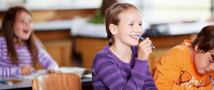 Smiling Girl in Purple Striped Sweater Seated in Classroom with Additional Students in Background